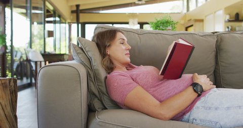 Relaxed caucasian pregnant woman lying on sofa and reading book. pregnancy, expecting baby and spending time at home.