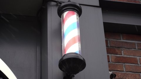 Red, white and blue barber pole on the side of the building with falling snow at winter. barbershop hairdresser traditional sign red blue and white spinning pole	