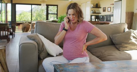 Stressed caucasian pregnant woman sitting on sofa, touching belly and having call. pregnancy, motherhood, expecting baby and spending time at home.
