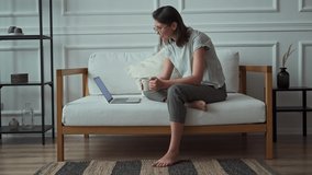 Young woman using laptop, relaxing and watching video while sitting on sofa at home