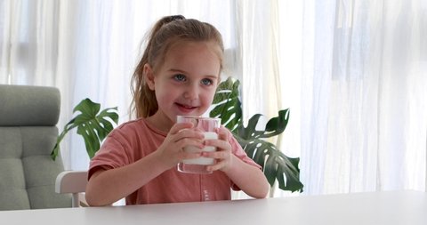 Cute cheerful girl drinks milk and stays with a mustache while sitting at a table at home