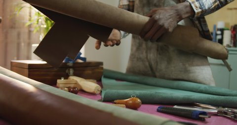 Hands of african american craftsman in apron unrolling leather in leather workshop. independent small business craftsman at work.