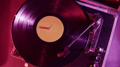Vinyl record close-up. Vintage old vinil black phonograph spinning. Retro music player in pink purple neon light.