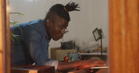 Thoughtful african american craftsman wearing glasses drinking coffee in leather workshop. independent small business craftsman at work.