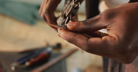 Hands of african american craftsman using tools to make a hole in leather workshop. independent small business craftsman at work.