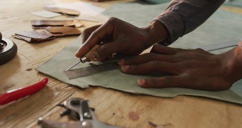 Close up of hands of african american craftsman cutting leather precisely in leather workshop. independent small business craftsman at work.