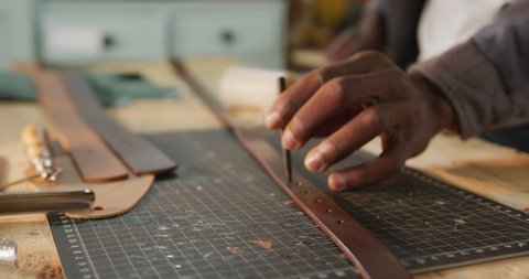 Hands of african american craftsman using tools to make a hole in leather workshop. independent small business craftsman at work.