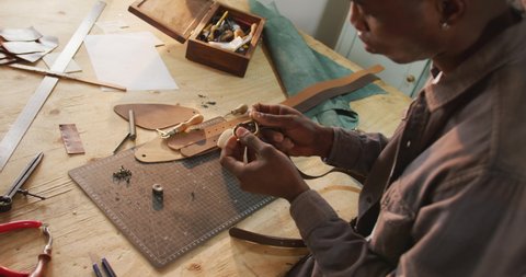 Focused african american craftsman using tools to make a belt in leather workshop. independent small business craftsman at work.