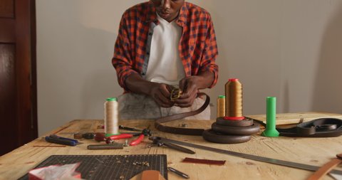 Focused african american craftsman using tools to make a belt in leather workshop. independent small business craftsman at work.