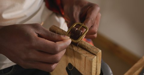 Hands of african american craftsman preparing belt in leather workshop. independent small business craftsman at work.