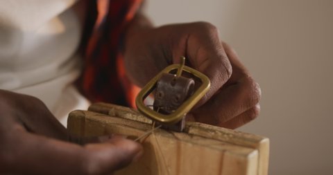 Close up of hands of african american craftsman preparing belt in leather workshop. independent small business craftsman at work.