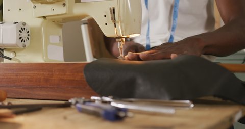 Hands of african american craftsman sewing leather in leather workshop. independent small business craftsman at work.