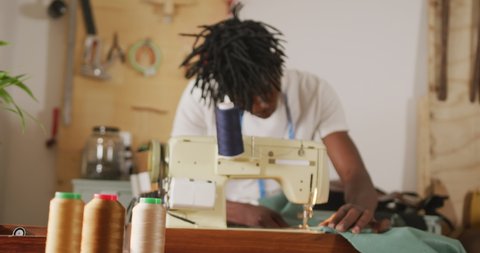 Focused african american craftsman with dreadlocks using sewing machine in leather workshop. independent small business craftsman at work.