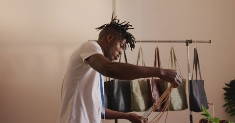 African american craftsman with dreadlocks arranging wallets and bags in leather workshop showroom. independent small business craftsman at work.