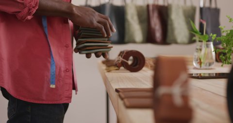Hands of african american craftsman arranging wallets on wooden surface in leather workshop. independent small business craftsman at work.