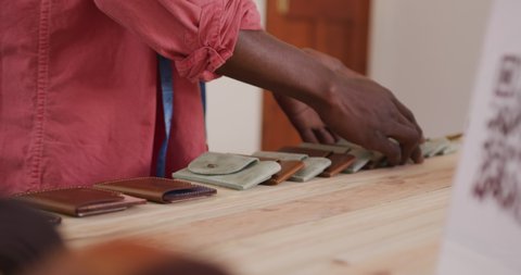 Hands of african american craftsman arranging wallets in leather workshop. independent small business craftsman at work.