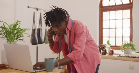 Happy african american craftsman with dreadlocks making phone call and using laptop in workshop. independent small business craftsman at work.