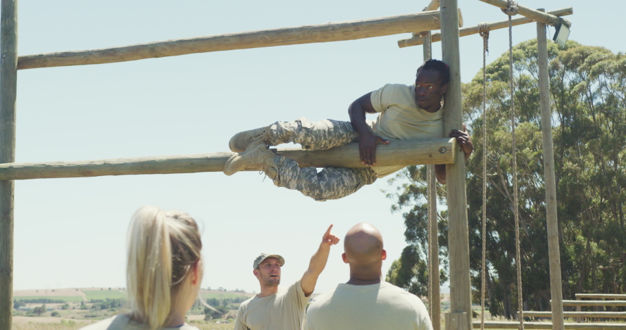 Diverse group watching fit african american male soldier with deadlocks climbing on obstacle course. healthy active lifestyle, cross training outdoors at boot camp.