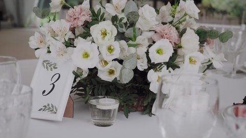 Wedding flowers on the white table. Card with three number. Glases with water. Wedding mood.