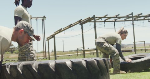 Fit diverse group of soldiers flipping tractor tyres on army obstacle course in the sun. healthy active lifestyle, cross training outdoors at boot camp.