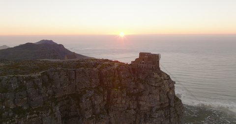 Aerial footage of Table Mountain flat summit with upper station of cable car. Fly around high rock above ocean coast at sunset. Cape Town, South Africa