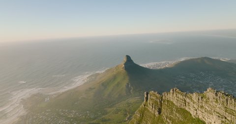 Aerial panoramic footage of mountains around town. Rugged sharp rock ridge on Table mountain and famous Lions Head mountain on ocean coast. Cape Town, South Africa
