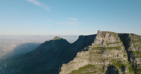 Massive rock mountain ridge with flatted top. Fly around famous Table mountain. One side lit by sun, one in shadow. Cape Town, South Africa