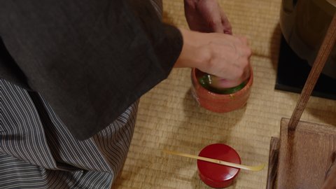Making powdered green tea ( matcha 抹茶 ) using  bamboo whisk (茶筅 chasen). The plan from above. Close-up of hands and chawan on the tatami. The treasure of Japanese culture is a traditional tea ceremony
