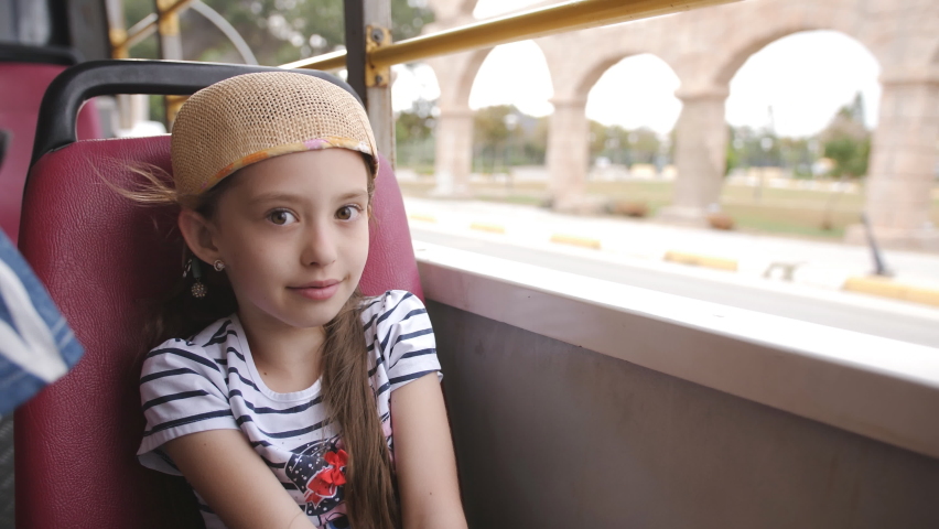 Little girl wrapped in a jacket on the bus with no Windows and looks outside.