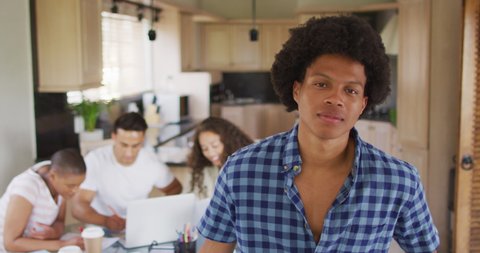 Happy african american man in kitchen with diverse friends working in background. technology and communication, flexible working from home.