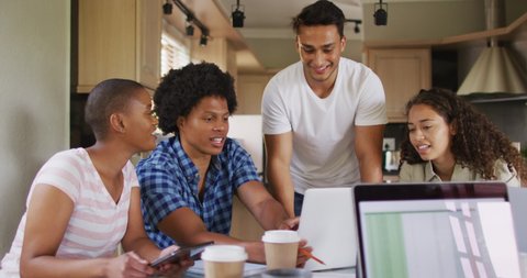 Group of diverse male and female friends in kitchen, laughing and working on laptops. technology and communication, flexible working from home.