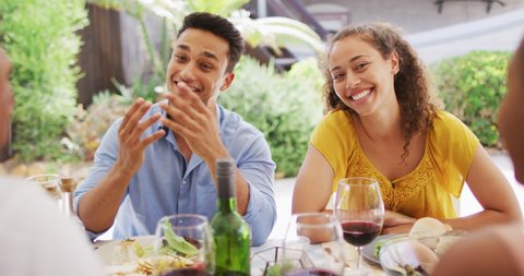 Diverse couple laughing with friends at dinner party on patio. hanging out with friends at home and garden.