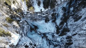 Spectacular aerial footage of mountain waterfall running through winter landscape.