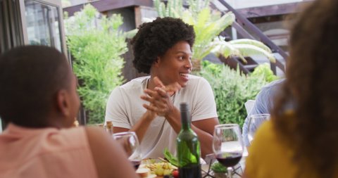 Happy african american man talking with friends at dinner party on patio. hanging out with friends at home and garden.