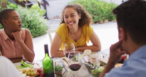 Happy biracial woman laughing with friends at dinner party on patio. hanging out with friends at home and garden.