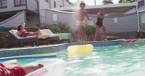 Group of happy diverse female and male friends ,jumping into swimming pool at pool party. hanging out with friends at home and garden.