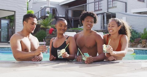 Group of diverse male and female friends toasting with drinks and laughing in swimming pool. hanging out with friends at pool party.