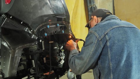 Unrecognizable mechanic using welding in a garage, repairing a car body, recovering from an accident