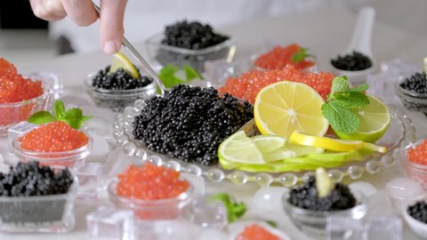 Hand with fork takes of caviar from the glass jar. Bowls with red salmon and black beluga sturgeon salted roe caviar on tasting table. Hands pick caviar in spoon Set delicious snacks on banquet