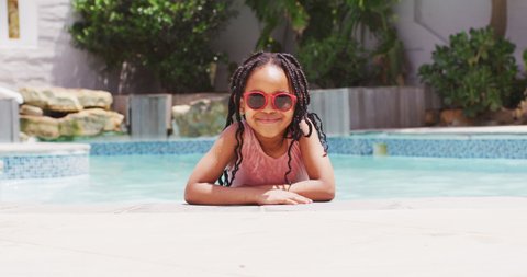 African american girl wearing sunglasses in swimming pool smiling at camera. childhood and vacations at home and garden.