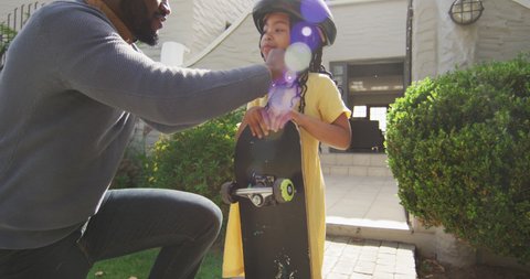 Happy african american father giving high five to daughter holding skateboard. quality family time together at home and garden.