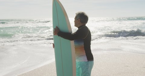 Back view of senior hispanic man standing on beach with surfboard. sporty, healthy and active retirement lifestyle.
