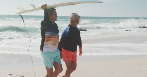 Side view of happy senior hispanic couple walking on beach with surfboard. sporty, healthy and active retirement lifestyle.