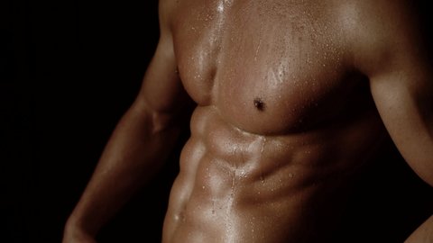 Strong athletic man showing muscular body and six pack abs on black background. Sexy naked torso, six pack abs. Male flexing his muscles. Close up on perfect abs. Strong bodybuilder with six pack.