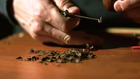 Man is putting tobacco in a vintage smoking pipe.