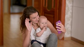 Loving tender young mother and her newborn baby making a selfie or video call to father. Mother and baby having video chat using smartphone sharing motherhood lifestyle with friend on social media.