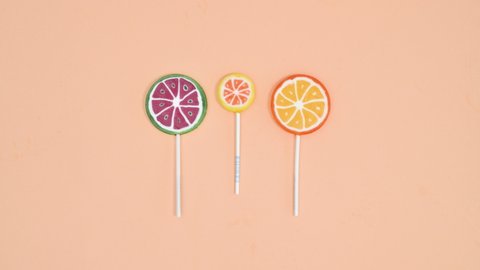 6k Creative stop motion animation of fruity lollipops on bright pastel orange background. Stop motion flat lay