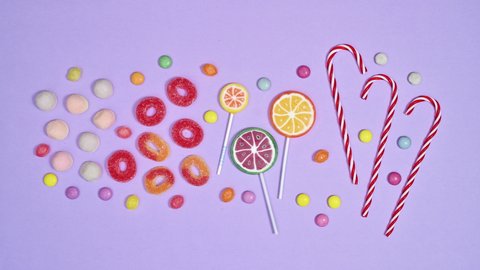6k Lollipops, colorful candies and gummy candies appear on pastel purple background. Stop motion flat lay