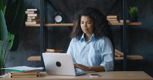 Young african american business woman video chatting with laptop at office. Female manager talking and looking at laptop screen while sitting at desk. Webcam webinar concept