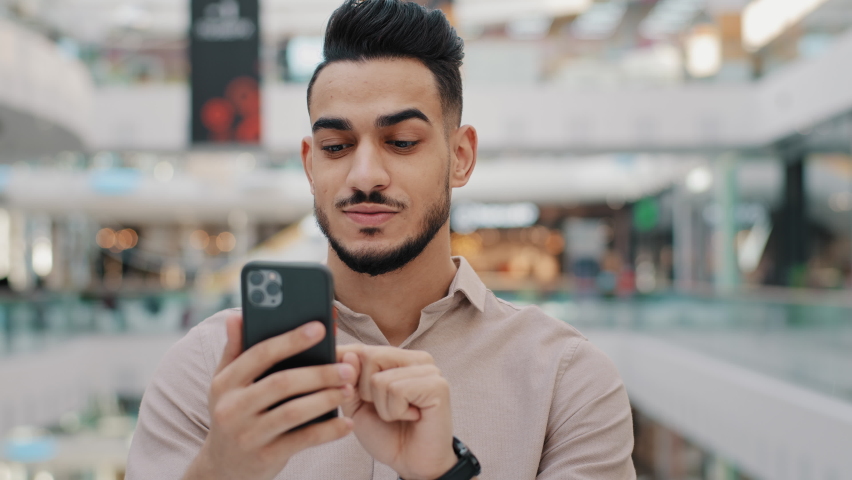 Happy smiling young arab male holding phone amazed joyful guy get cash prize lottery winner hispanic man applying for quick loan using banking app on modern smartphone shocked instant receiving money Royalty-Free Stock Footage #1086912863